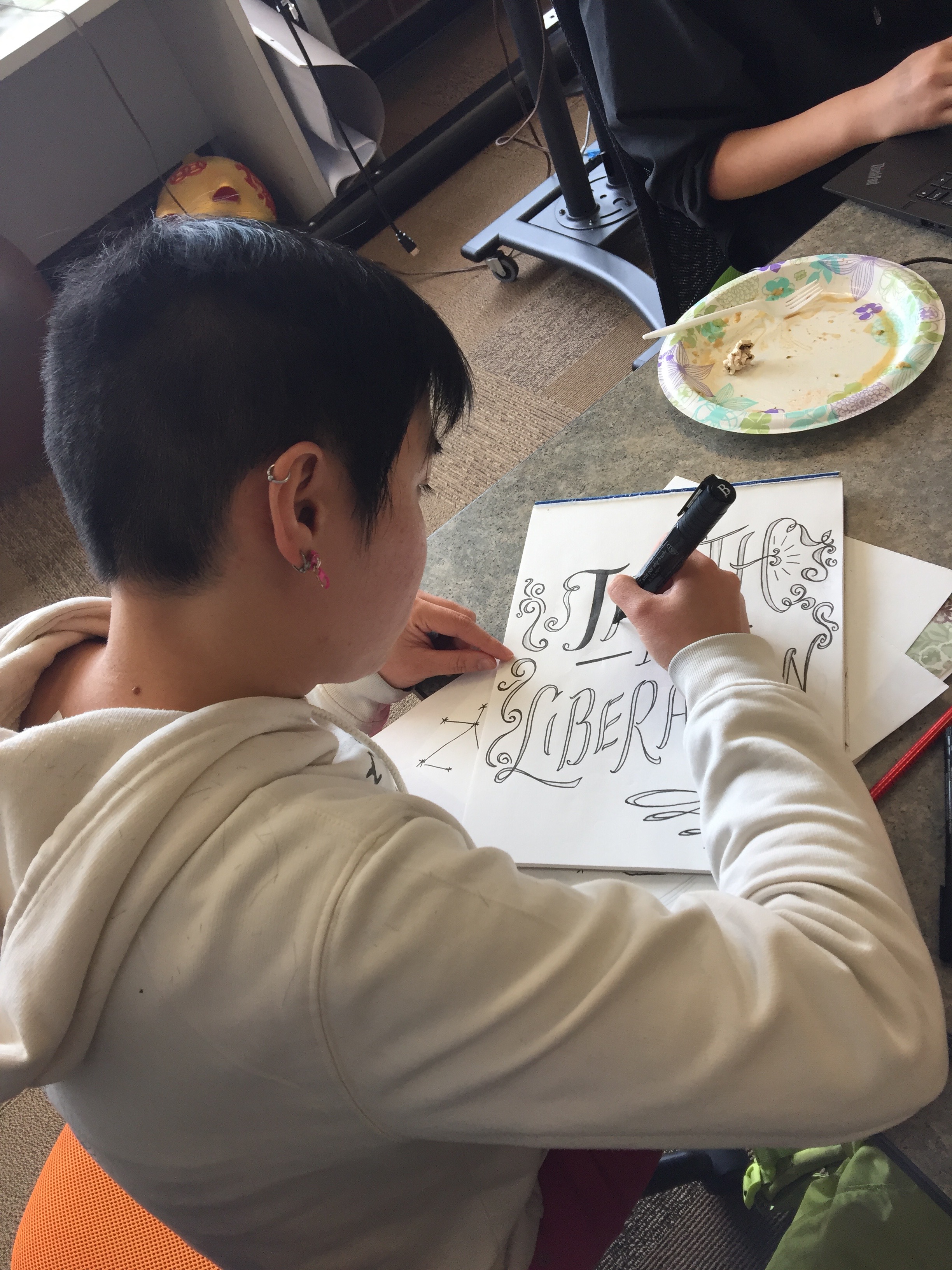 Image Description: A person with short hair and a white sweatshirt is drawing an image with the words "Truth is Liberation"