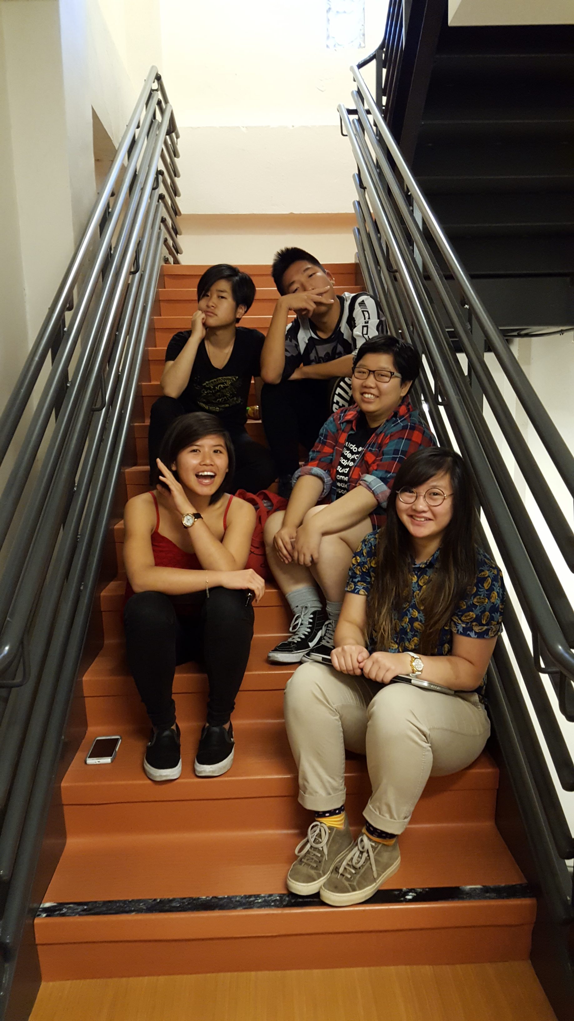 Image Description: Five APIENC Summer Interns sit on steps in a stairwell. They all make a range of silly, smiling, and serious faces to the camera. 