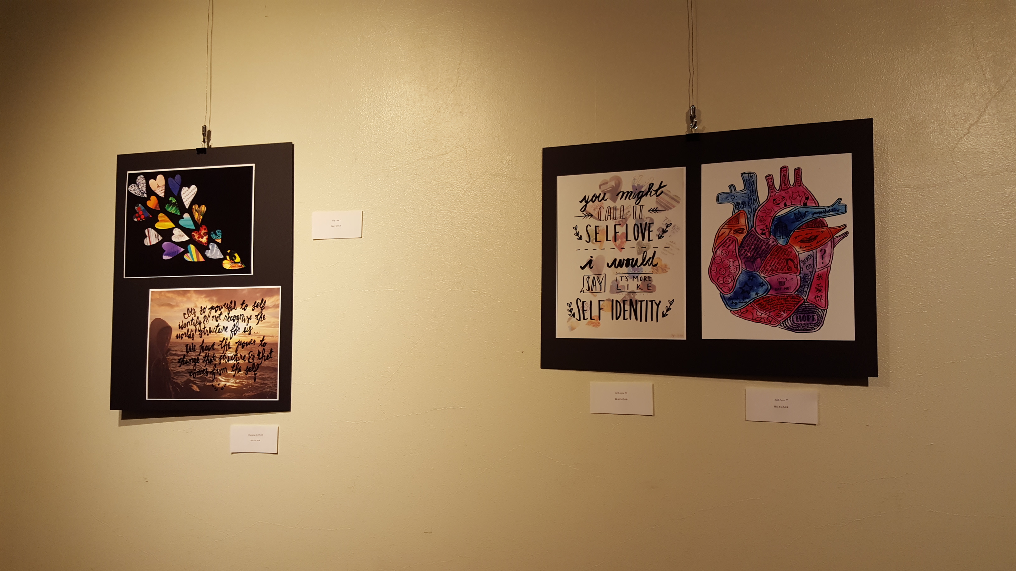 Image Description: Artwork from the Artist Collective Exhibit hangs on the wall. Four prints are arranged on two black backgrounds. 