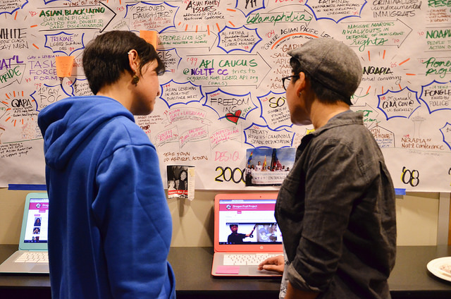 Image Description: Two APIENC community members browsing the Dragon Fruit Project Digital Portal on a Google Chromebook; a historical timeline of LGBTQ API movements is in the background