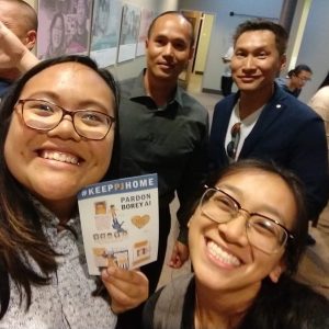 Image description: 2018 summer organizers Teo and Julie smile at the camera. Teo is holding a postcard that reads "#KeepPJHome". Behind them stand Borey PJ Ai and Eddie Zheng of APSC